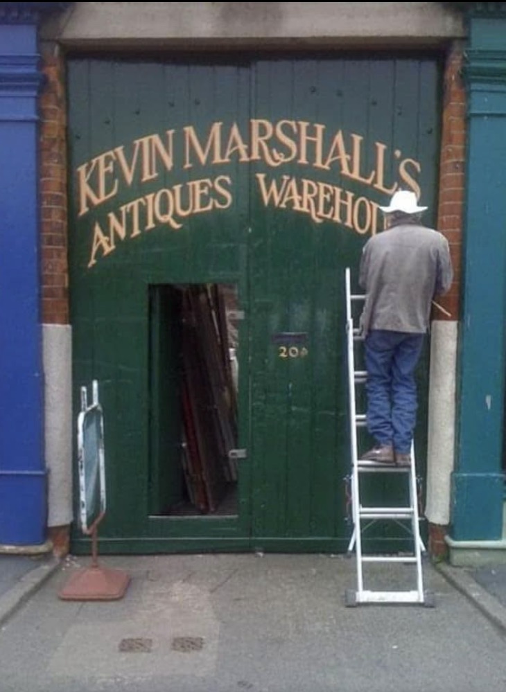 Kevin up a ladder, repainting the lettering above the big green warehouse doors